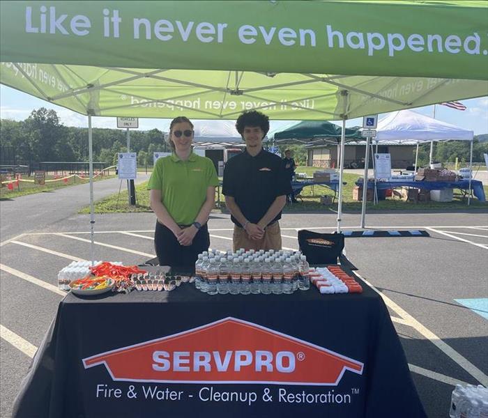 two SERVPRO workers standing infront of a table with a black tablecloth with water bottles and promo items displayed